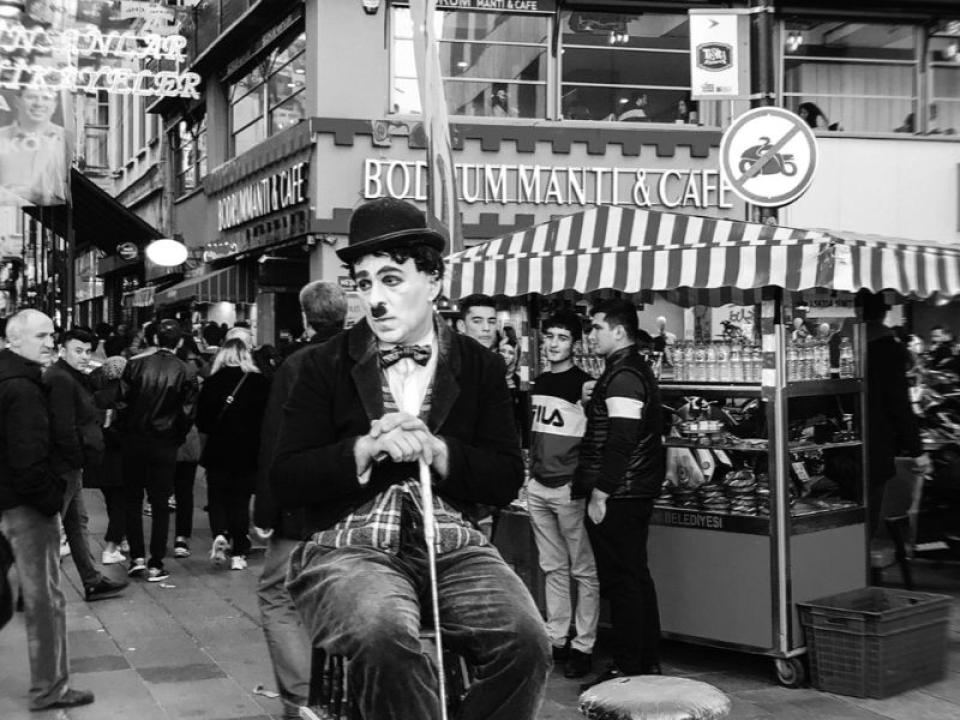 black and white photo of a Charlie Chaplin actor sitting on a high chair observing a busy street
