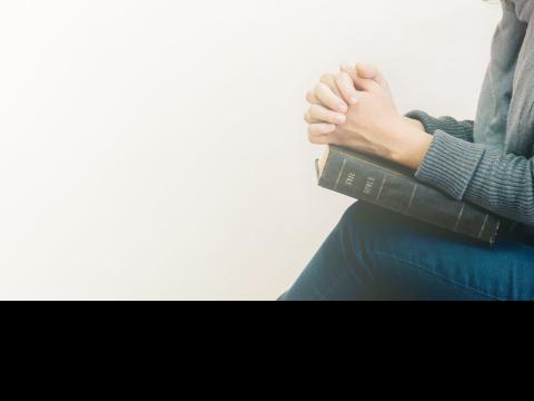 woman praying with clasped hands on open book