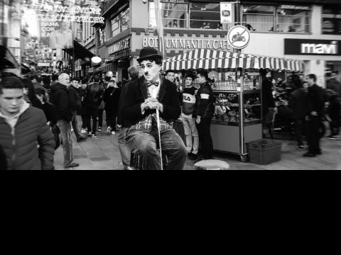 black and white photo of a Charlie Chaplin actor sitting on a high chair observing a busy street