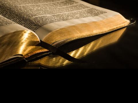 Old Bible with gold leafed pages and ribbon marking place open on burnished tabletop