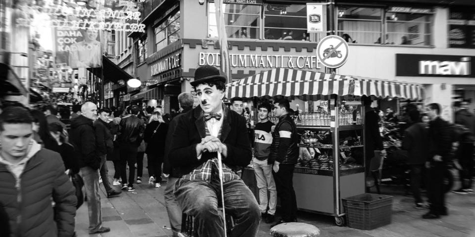 black and white photo of a Charlie Chaplin actor sitting on a high chair observing a busy street