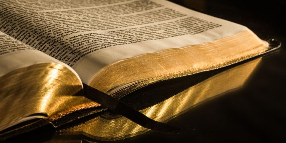 Old Bible with gold leafed pages and ribbon marking place open on burnished tabletop
